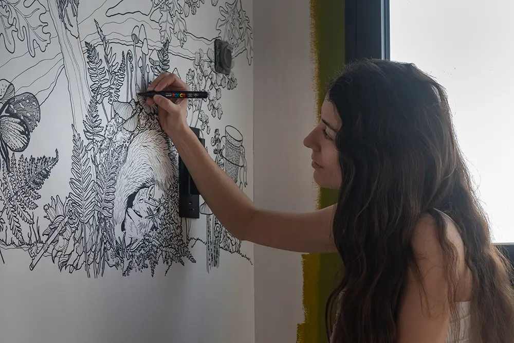 Aménagement intérieur d'une tiny house. Apolline Geronimi en train de dessiner l'une des fresques murales de l'espace séjour.