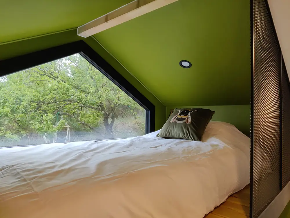 Aménagement intérieur d'une tiny house. Couchette mezzanine invité lit simple et sa vue sur les chênes alentours.