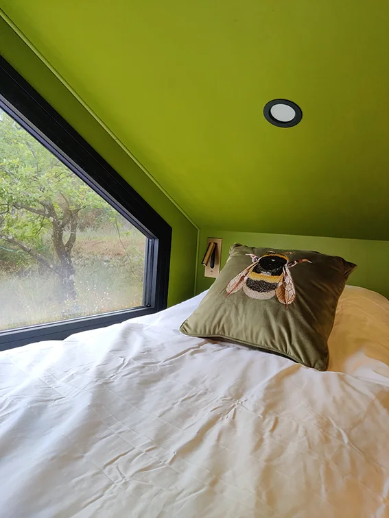 Aménagement intérieur d'une tiny house. Photographie du coussin velours vert avec broderie bourdon de la couchette mezzanine simple.