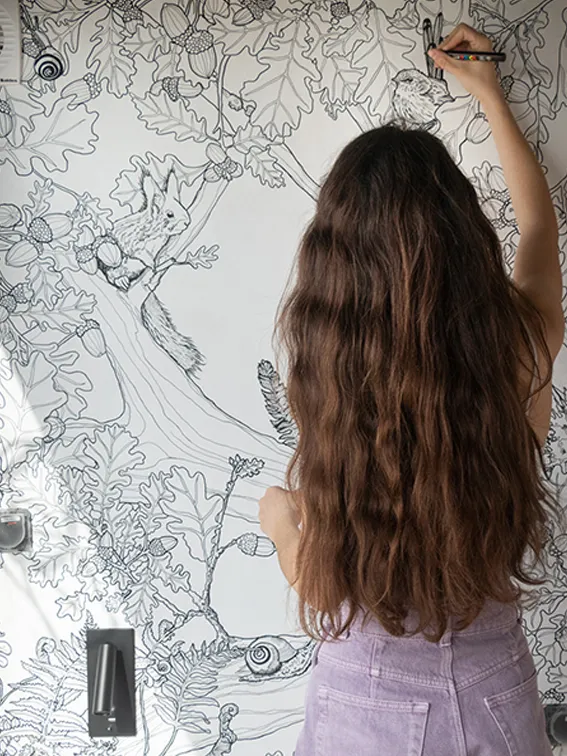 Aménagement intérieur d'une tiny house. Apolline Geronimi en train de dessiner la fresque murale sur mesure qui sera située au fond d'une des bibliothèque de l'espace canapé.