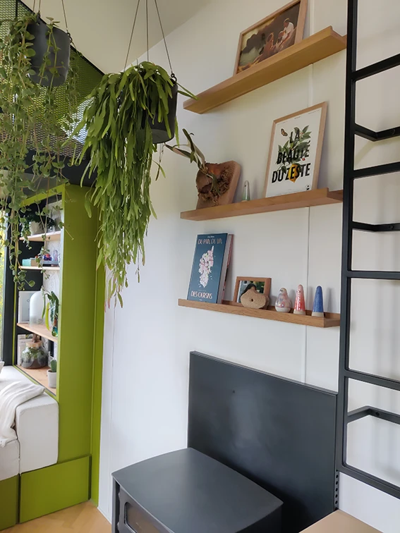 Aménagement intérieur d'une tiny house. Etagère et décorations au dessus du poêle à bois.