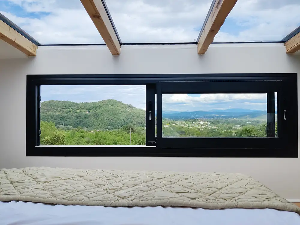 Aménagement intérieur d'une tiny house. Fenêtre coulissante bandeau dans l'espace nuit chambre et fenêtre de toit.