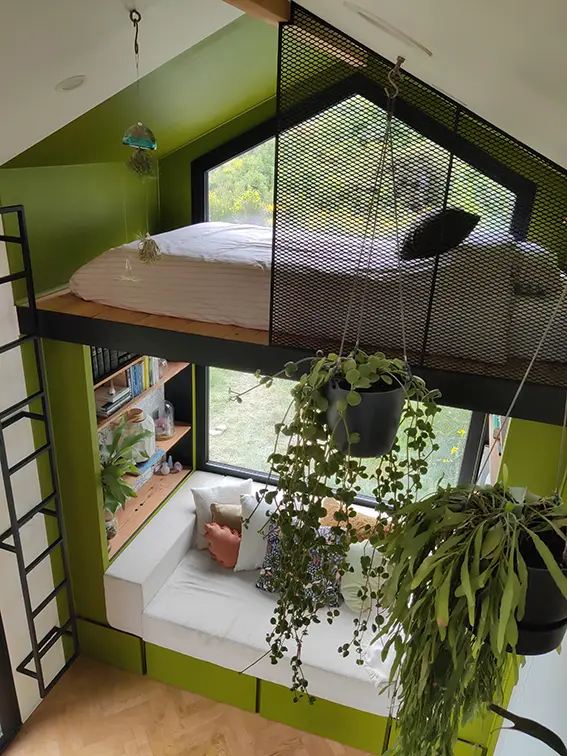 Aménagement intérieur d'une tiny house. Vue de haut de la couchette simple sur mezzanine, de la niche verte regroupant également l'espace canapé.