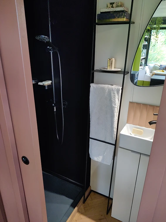 Aménagement intérieur d'une tiny house. Salle d'eau avec vue vers douche et lave mains.