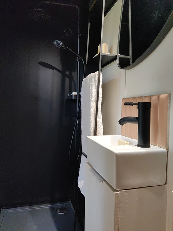 Aménagement intérieur d'une tiny house. Douche métallique noire et lave mains avec son miroir.