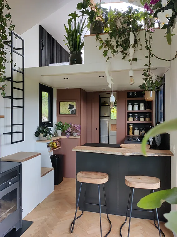 Aménagement intérieur d'une tiny house. Vue d'ensemble vers la cuisine, la salle d'eau et la mezzanine couchage double.